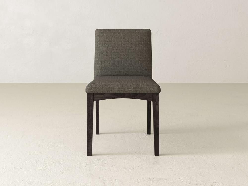 The Klein Dining Chair, by James & James, stands on a light-textured floor with a plain white background. It features maple wooden legs and a cushioned gray-green seat with an elegantly upholstered back for added comfort and style.