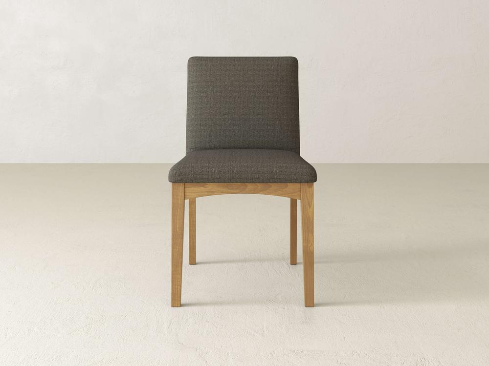 The Klein Dining Chair by James & James features maple wooden legs, a padded upholstered back, and a dark gray fabric seat against a minimalist off-white backdrop.