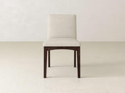 The Klein Dining Chair by James & James features a cream upholstered seat and backrest, elegantly supported by maple wooden legs against a plain, light-colored wall and floor.