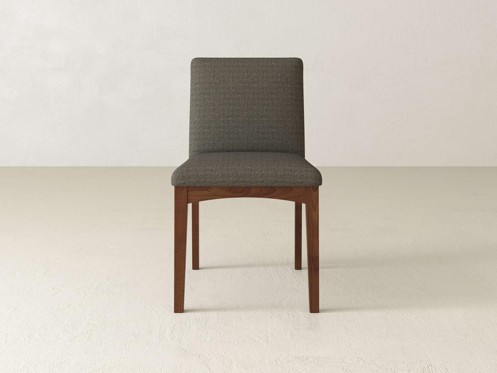 The Klein Dining Chair by James & James, with its grey cushioned backrest and seat, stands elegantly against a white wall on a light floor. Its modern design is complemented by maple wooden legs, adding warmth to its sleek look.