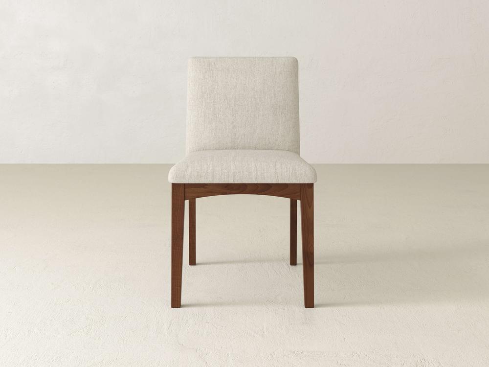 The Klein Dining Chair from James & James showcases a light beige upholstered seat and backrest, supported by four maple wooden legs. It elegantly complements a neutral-toned room with a smooth, light-colored floor.