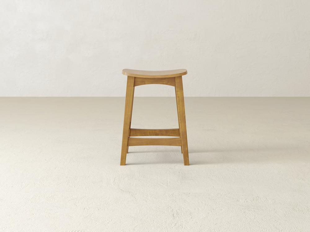 The James & James Weston Stool, crafted from maple hardwood, features a contoured seat and footrest. Its simple, minimalist design stands out beautifully on a plain light floor against a matching wall.