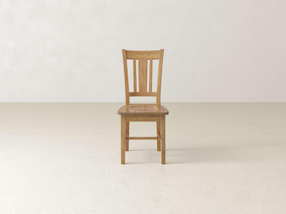 The William Dining Chair - Tuscany by James+James stands alone on a light-colored, smooth floor. Featuring a slatted backrest and a polished finish, the chair is centered in front of an empty, plain off-white wall. The setting is minimalistic and clean.