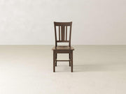 The William Dining Chair - Tobacco by James+James is centered in a minimalist room with light-colored walls and flooring. This dark wooden chair features a slatted backrest, four straight legs, and a simple yet classic design.