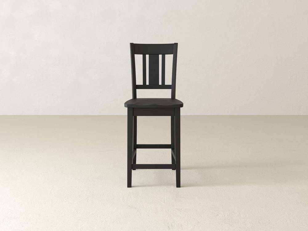 The William Stool by James & James is a black wooden chair exuding timeless sophistication, set against an off-white backdrop. It features a slatted backrest and four legs, connected by a horizontal support for added stability.