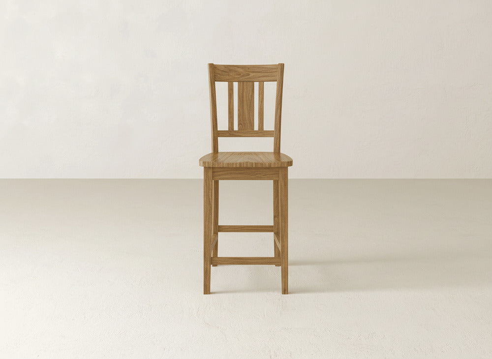 The William Stool by James & James is a handcrafted wooden barstool featuring a slatted backrest and square legs, elegantly displayed on a light floor against an off-white wall—perfect for enhancing any home décor.