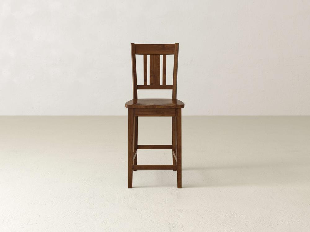 The William Stool by James & James features a wooden slatted backrest and a rich brown finish, positioned against an off-white background. This sophisticated home decor piece has a simple, sturdy design and rests elegantly on a flat surface.