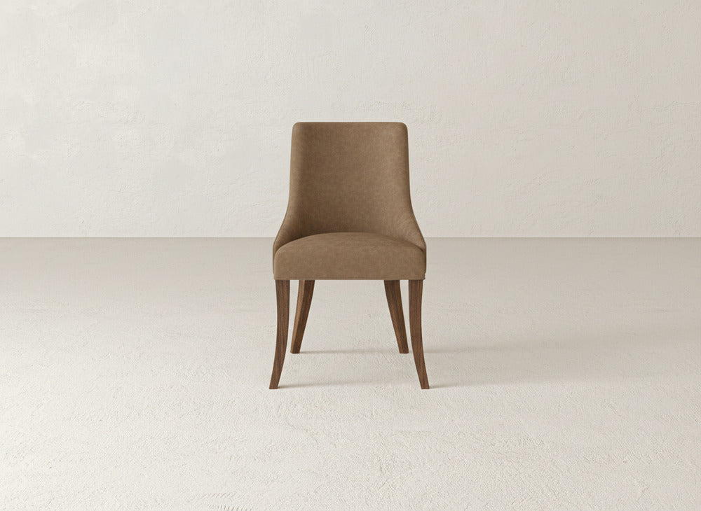 The Willow Dining Chair by James+James, featuring brown upholstery and wooden legs, sits on a light floor with a neutral textured wall in the background.