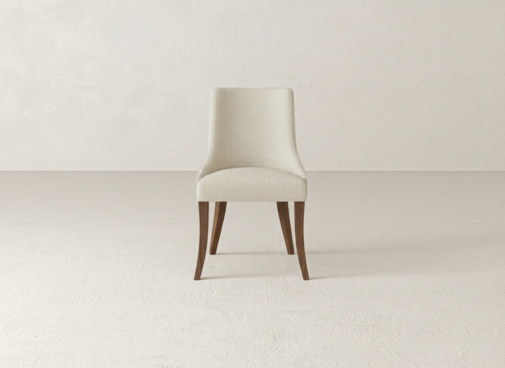 A James+James Willow Dining Chair featuring light upholstery and dark wooden legs is positioned in a minimal, empty room with pale floors and walls.