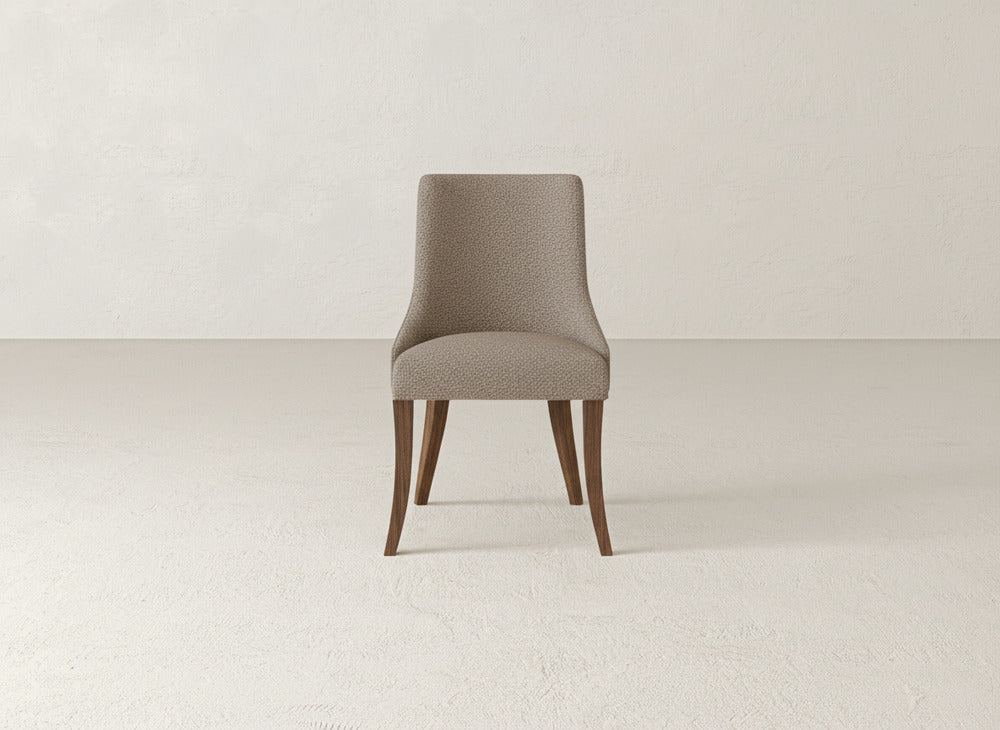 A James+James Willow Dining Chair with light gray fabric and wooden legs stands on a light, textured floor against a plain off-white wall.
