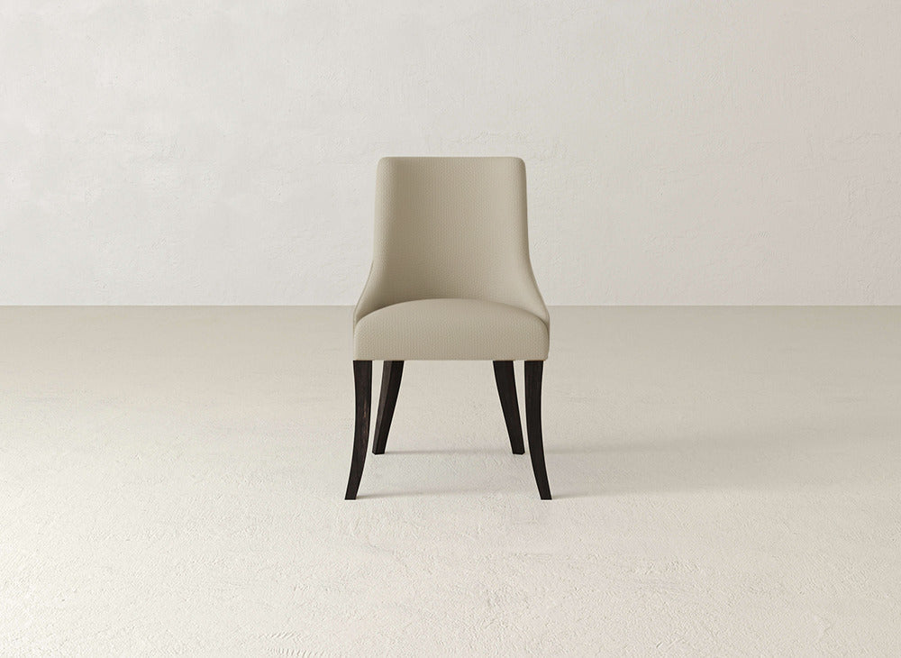 The Willow Dining Chair by James+James, featuring beige upholstery and dark wood legs, is centered against a plain, light-toned wall and floor for a minimalist, modern look.