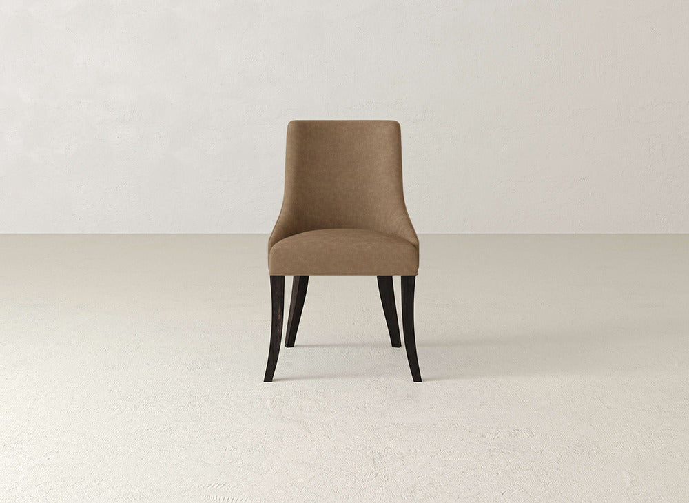 A single James+James Willow Dining Chair, featuring brown upholstery and dark wooden legs, is centered in a minimalist, light-toned room with a textured wall and floor.