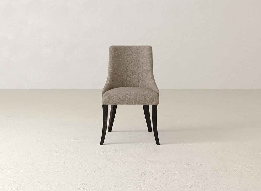 A single James+James Willow Dining Chair with beige upholstery and dark wooden legs sits centered in an empty room with light walls and flooring.