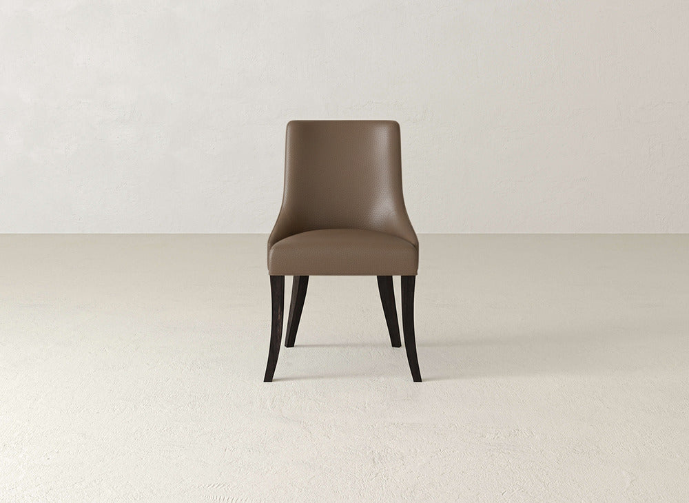 A single brown James+James Willow Dining Chair with dark wooden legs is centered in an empty, light-colored room with a plain textured wall and floor.