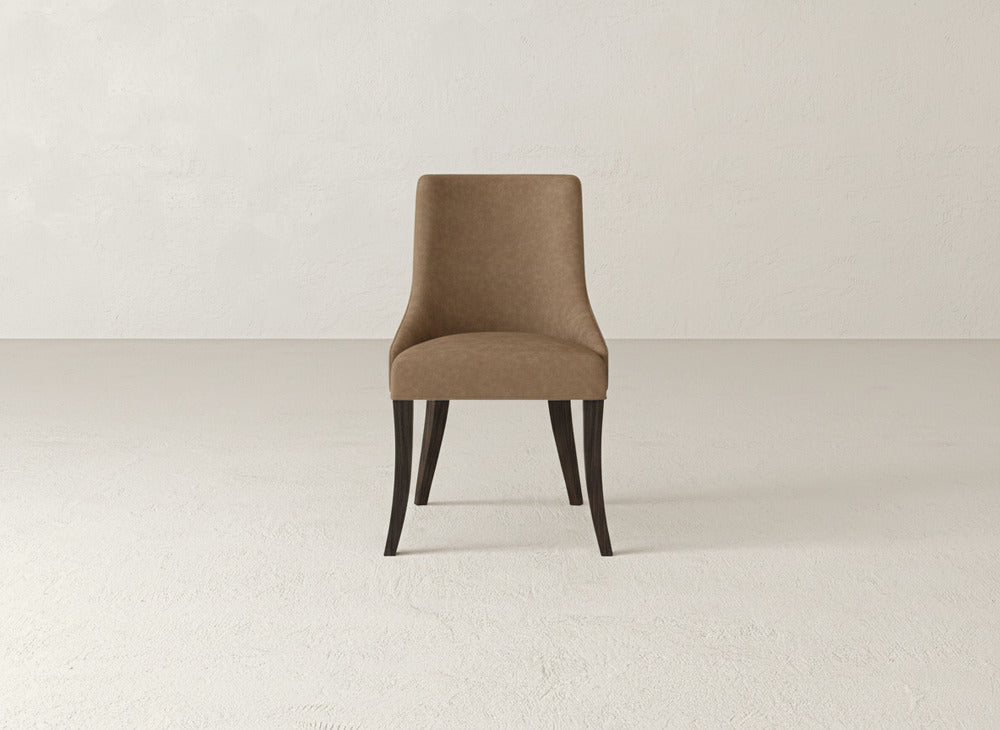 A brown James+James Willow Dining Chair with dark wooden legs is centered in a minimalist room with light-colored walls and floors.