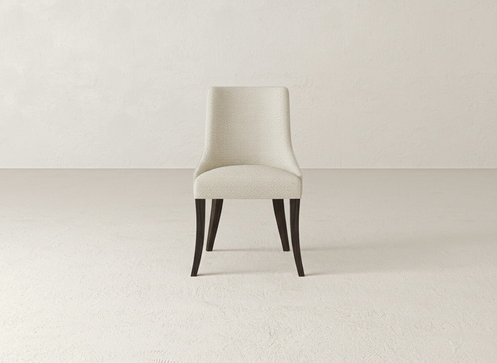 A modern James+James Willow Dining Chair with light fabric and dark wooden legs sits centered in a minimalist, neutral-toned room featuring a textured wall and floor.