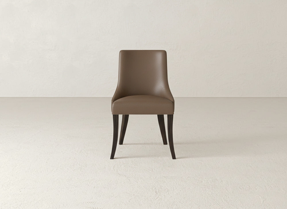 A brown James+James Willow Dining Chair with modern upholstery and dark wooden legs sits centered in a minimal, empty room with light-colored textured walls and floor.