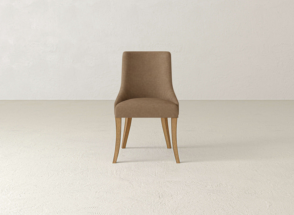 A brown Willow Dining Chair by James+James, featuring light wood legs, is centered in an empty, neutral room with textured walls and floor.