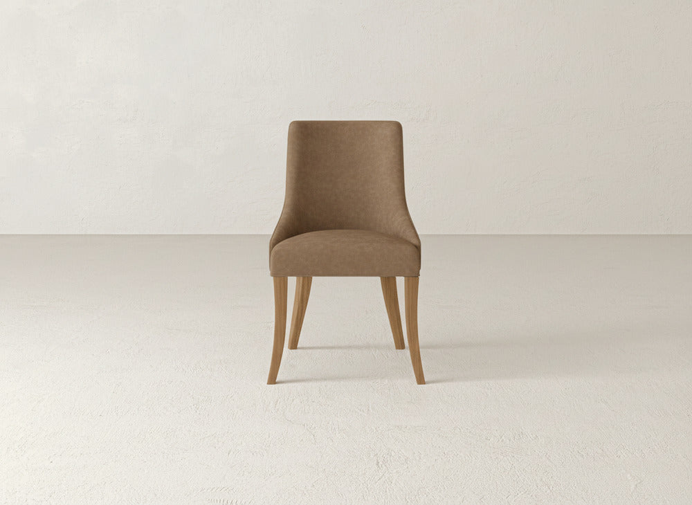 A single James+James Willow Dining Chair, featuring a brown upholstered seat and backrest with light wooden legs, is positioned in an empty, neutral-toned room with textured walls and flooring.