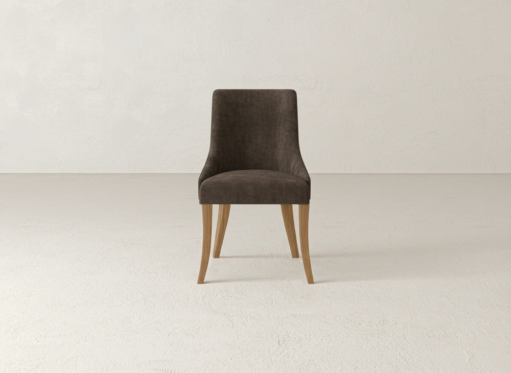 The James+James Willow Dining Chair features a dark upholstered seat and backrest with light wooden legs, set on a light floor against an off-white minimalist wall.