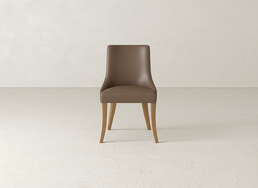 A brown James+James Willow Dining Chair with wooden legs is centered in an empty, light-colored room with a plain wall and floor.