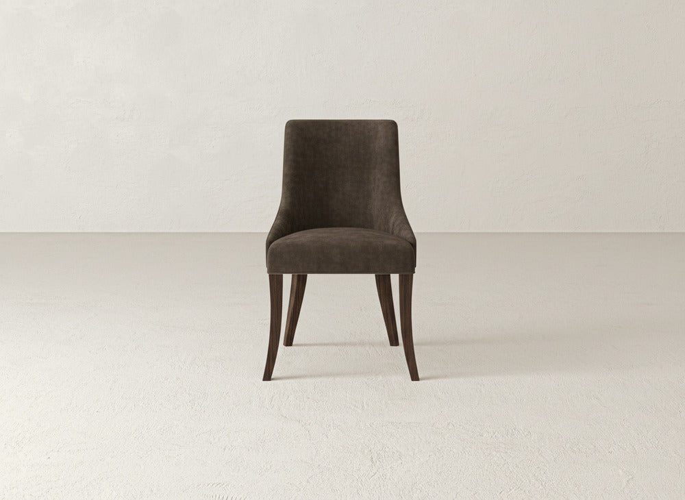 A single James+James Willow Dining Chair with dark brown upholstery and wooden legs is centered in a minimal, light room featuring textured walls and flooring.