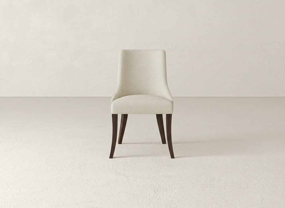 A beige James+James Willow Dining Chair with dark wooden legs is centered in an empty, light-toned room with textured walls and floors.