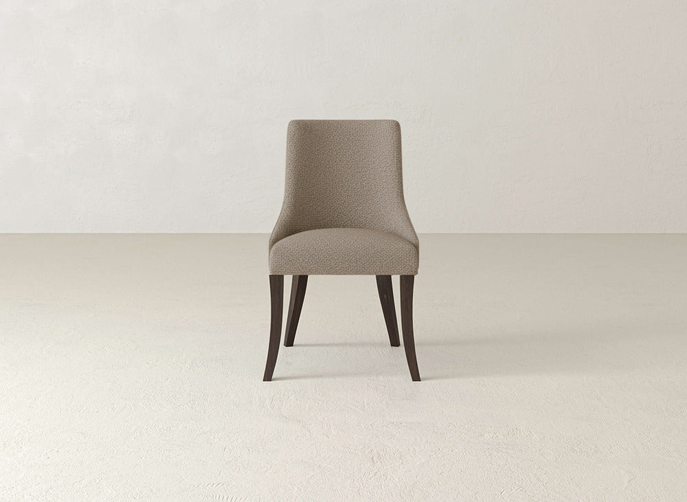 The Willow Dining Chair by James+James is a modern upholstered chair featuring curved dark wooden legs and a beige fabric seat and backrest, perfect for minimalist, light-colored spaces.