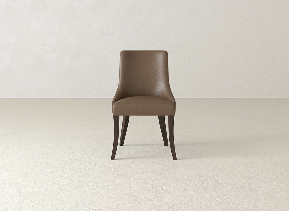 The James+James Willow Dining Chair features brown upholstery, a curved backrest, and dark wooden legs, shown on a light textured floor with an off-white wall background.