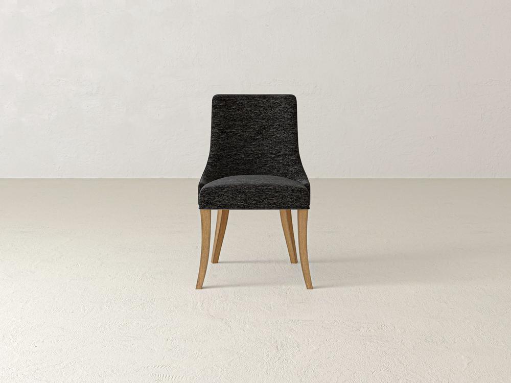 A modern chair with a dark gray, textured fabric seat and backrest, featuring wooden legs, is centered in a minimalistic white room with a light-colored floor.