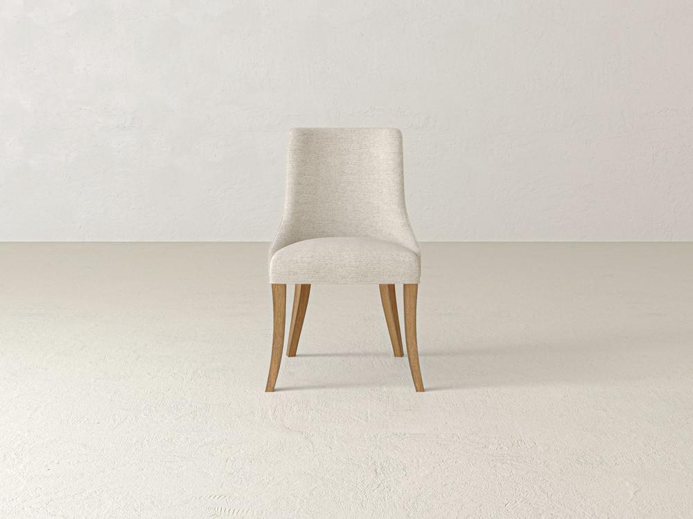 A minimalist chair with a beige fabric seat and back, featuring light wooden legs, stands alone in a neutral-colored room with a textured wall and floor.