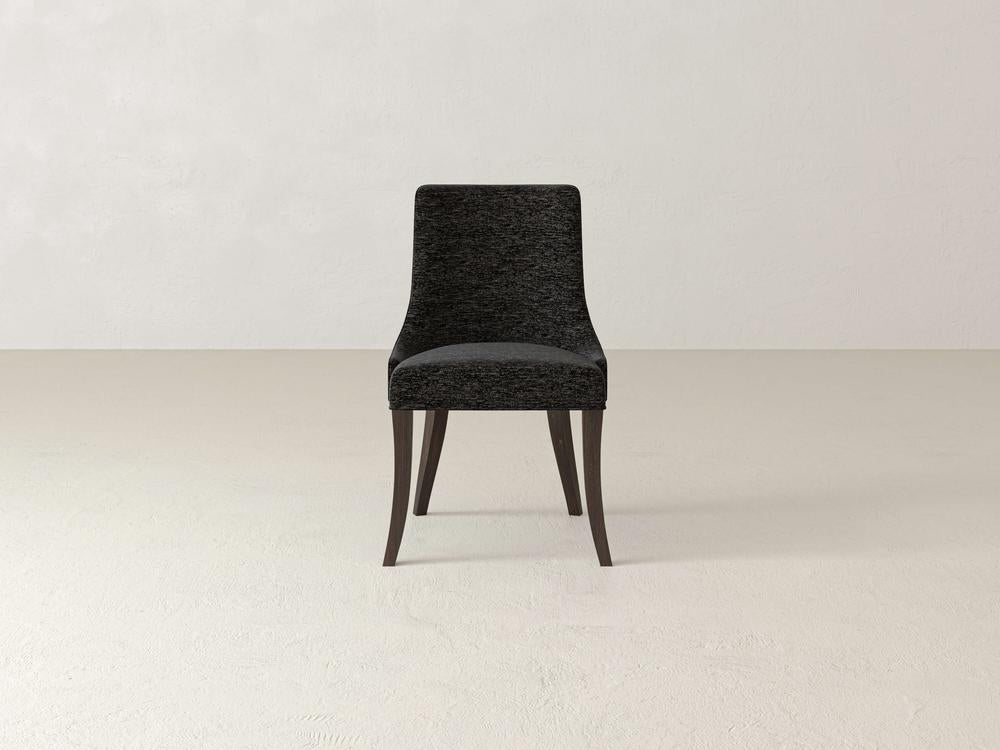 A dark upholstered chair with a high backrest and wooden legs stands against a plain off-white background. The chairs minimalist design features sleek, slightly curved legs.