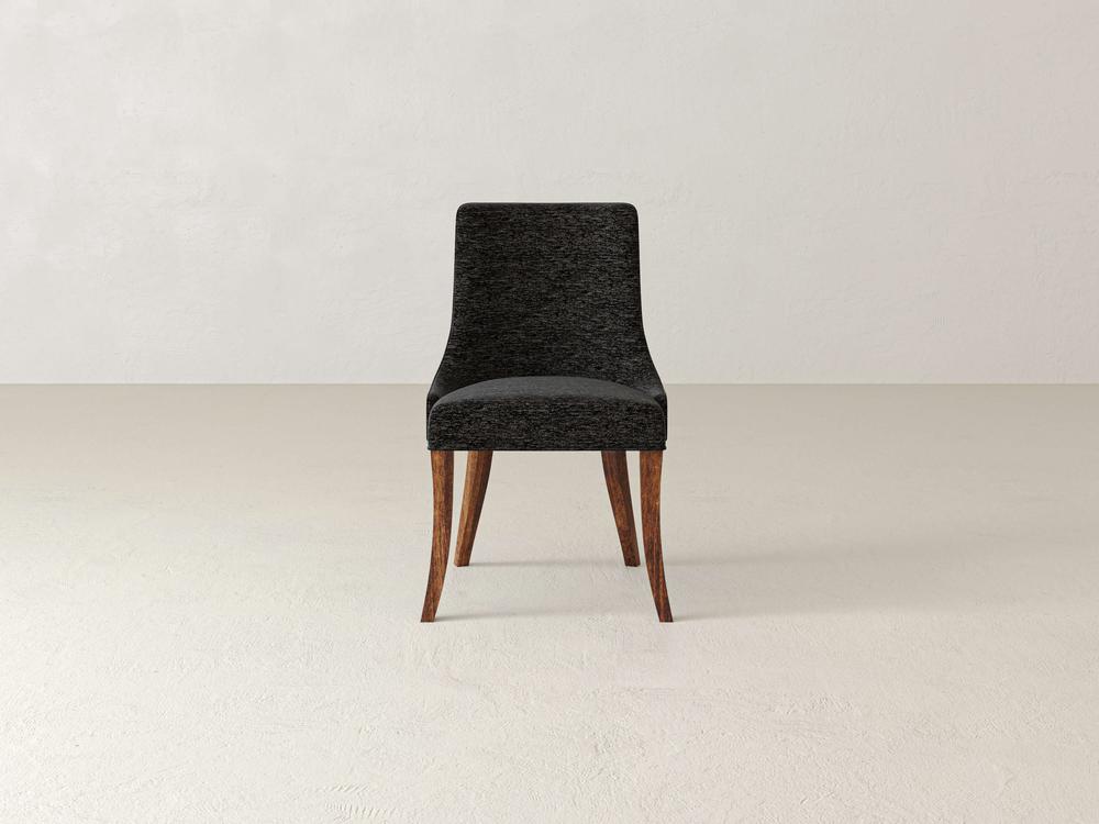 A dark upholstered chair with wooden legs sits on a light-colored floor against a plain, light-toned wall. The chair has a simple, modern design with a cushioned seat and backrest.
