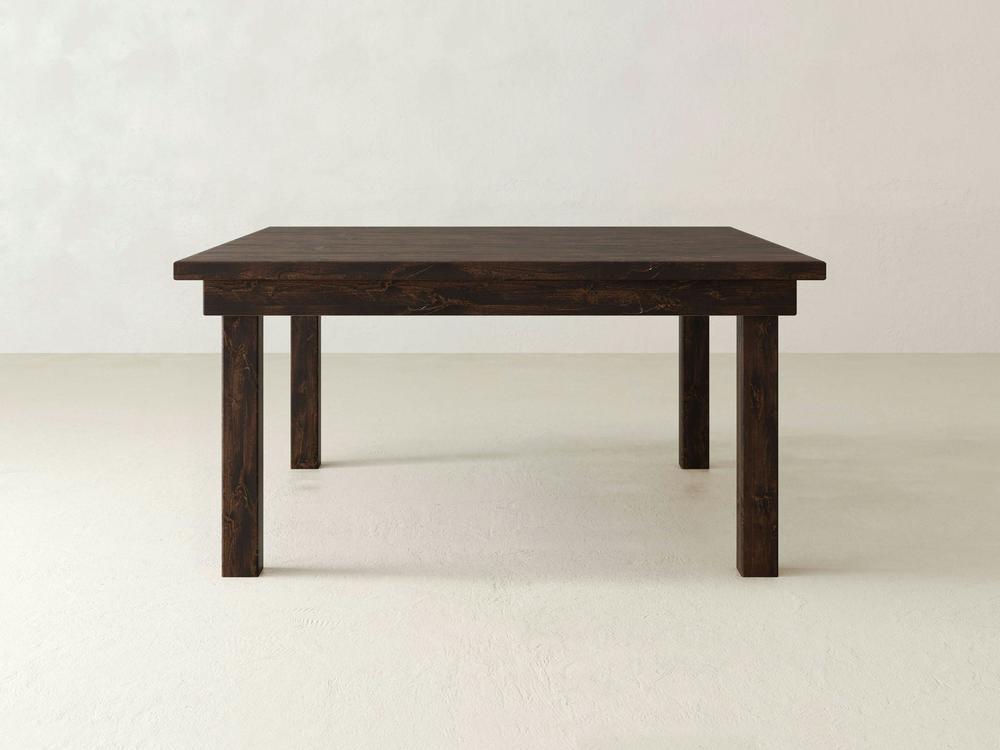 A Farmhouse Square Dining Table from James+James is placed against a plain light-colored background, showcasing its sturdy and minimalist design. The solid hardwood surface and legs display a natural wood grain texture, adding a touch of rustic elegance.