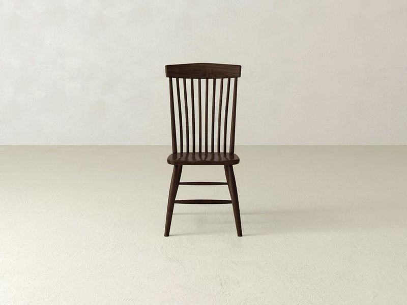 The Harper Side Dining Chair by James & James features a classic design with dark wood and vertical backrest slats. It sits centered on a light floor against a pale wall, showcasing its handcrafted elegance.