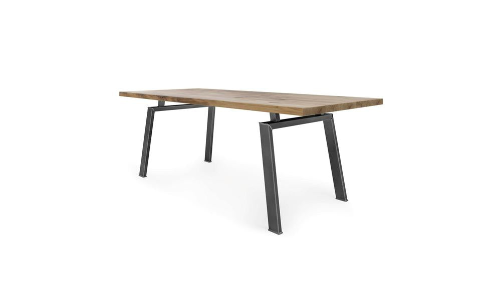 The Fulton Dining Table - Harvest Wheat by James+James features a rectangular, modern design with a light wooden tabletop and black, angular metal legs. This table boasts a minimalistic aesthetic, with uniquely angled legs that create an industrial look. The image showcases the table against a white background.