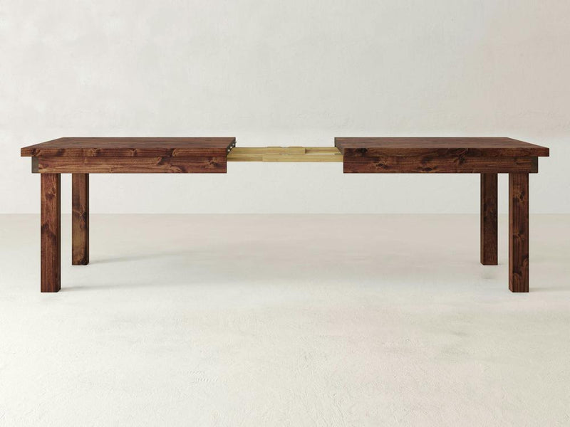 A close-up of the Farmhouse Expandable Dining Table - Tuscany by James+James, showcasing a natural knot and wood grain patterns. The image highlights the texture and color variations in the medium brown wood with a smooth finish.