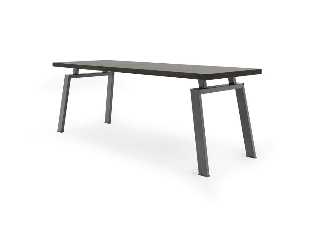 The Fulton Desk - Charred Ember by James+James features a sleek, dark rectangular tabletop supported by four black, angled metal legs positioned at each corner and slightly splayed outward for a contemporary design. This modern desk embodies a minimalist and industrial aesthetic.