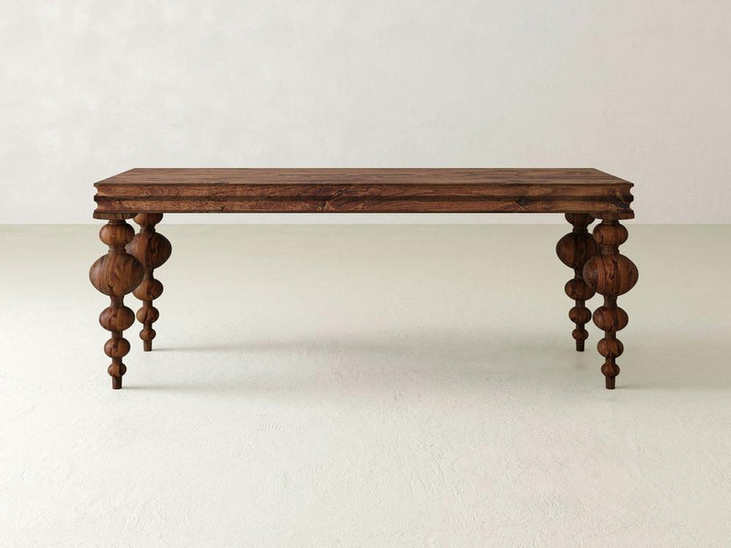 The Olivia Sofa Table - Tuscany by James+James features a rectangular wooden tabletop and intricately carved legs adorned with a series of bulbous shapes. The table boasts a rustic, natural wood finish and is photographed against a plain, light-colored background.