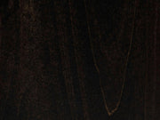 A close-up of the Charred Ember on Alder Sample by James+James reveals a dark, textured surface with subtle variations in color and grain patterns. A faint V-shaped lighter streak adds depth to the otherwise rich and smooth finish, which has a deep, almost black appearance.