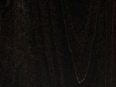 A close-up of the Charred Ember on Alder Sample by James+James reveals a dark, textured surface with subtle variations in color and grain patterns. A faint V-shaped lighter streak adds depth to the otherwise rich and smooth finish, which has a deep, almost black appearance.