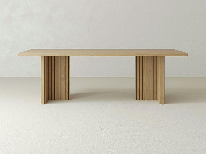 The Francesca Dining Table - Satin by James+James is centered in the image. This minimalist table features a rectangular top and two sturdy legs composed of vertical slats, creating a modern, sleek aesthetic. The background is light and plain, highlighting the table's clean lines and natural wood finish.