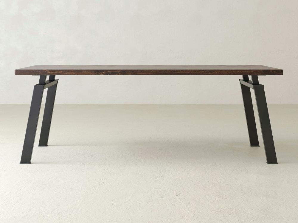 The Fulton Desk - Tobacco by James+James is a minimalist, modern desk featuring a rectangular wooden top with a dark wood finish and angled metal legs in a gray color. The desk boasts an open design with a simple, sturdy frame, perfect for any contemporary space.