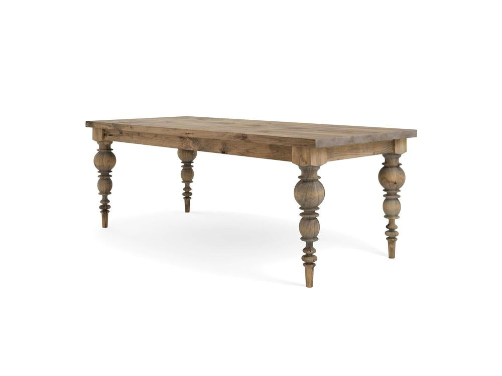 The Bailey Dining Table - Harvest Wheat by James+James is a wooden dining table with a rustic design featuring a rectangular top and intricately turned legs. The natural wood finish showcases the grain and texture, giving it a vintage, farmhouse look. The legs are tapered and decorated with carved details.