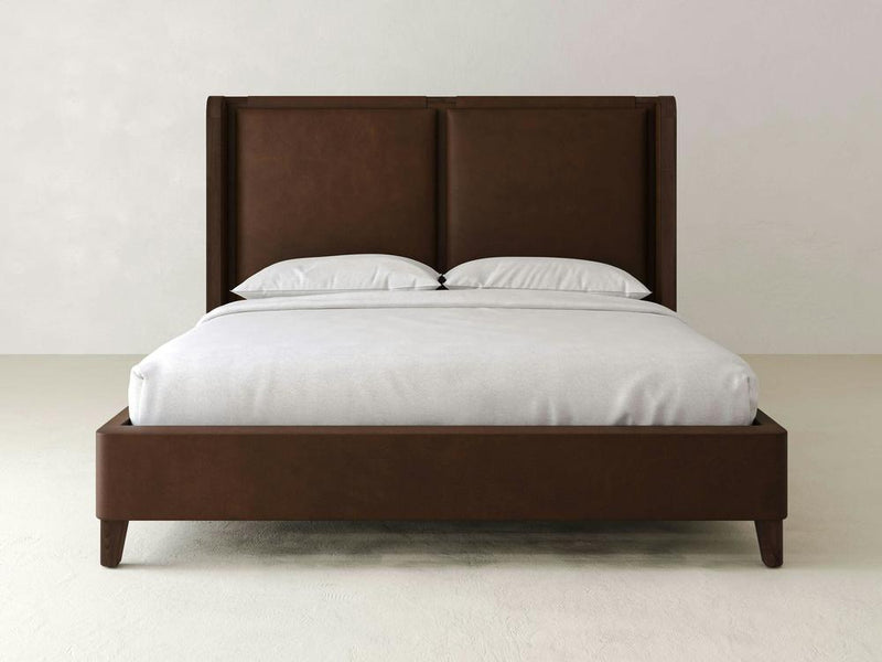 The James & James Holden Bed – Leather boasts a contemporary design with a double bed and tall headboard, elegantly made with white sheets and pillows. Crafted from solid maple wood, it complements light-colored walls and a smooth floor for a sleek, modern look.