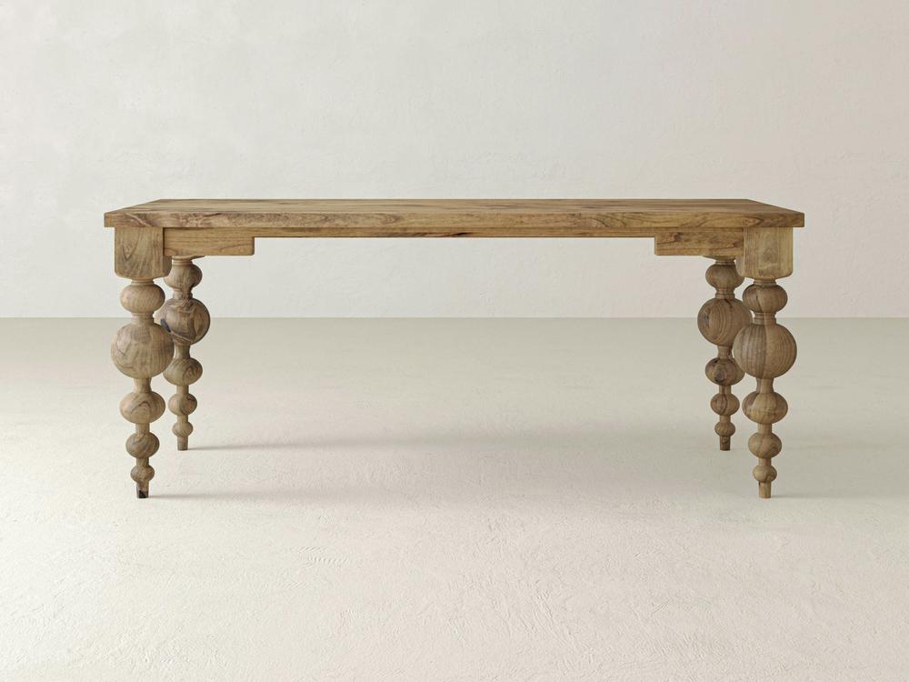 A close-up of the Olivia Desk in Harvest Wheat by James+James showcases a beautiful wooden surface with visible grain patterns and a prominent knot in the upper center. The desk features a natural light brown color with subtle variations in tone and a smooth texture.