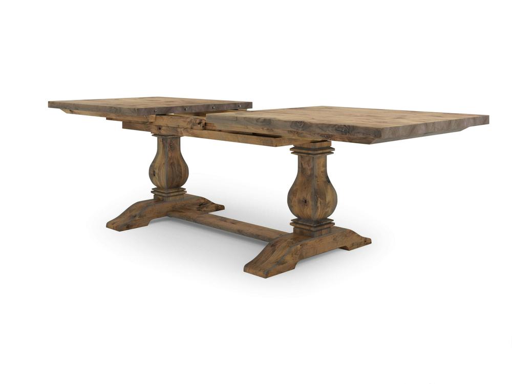 The Heirloom Expandable Dining Table - Harvest Wheat by James+James is a rustic wooden dining table featuring a split tabletop design with two large rectangular planks on top. It is supported by two ornate, turned pedestal legs connected by a central, sturdy wooden beam and showcases a natural, distressed finish.