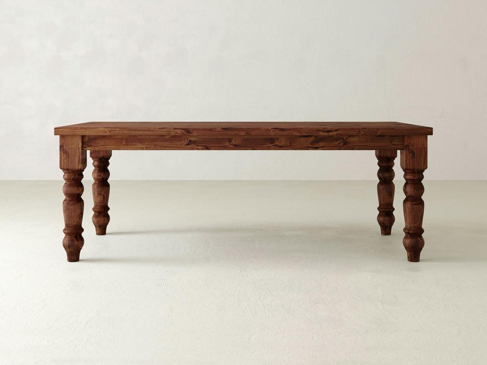 Introducing the James+James Baluster Dining Table: Featuring intricately carved, turned legs and a smooth, polished surface, this table is expertly handcrafted from fine wood. Set against a plain, light-colored background, its design exudes a timeless classic and rustic charm.