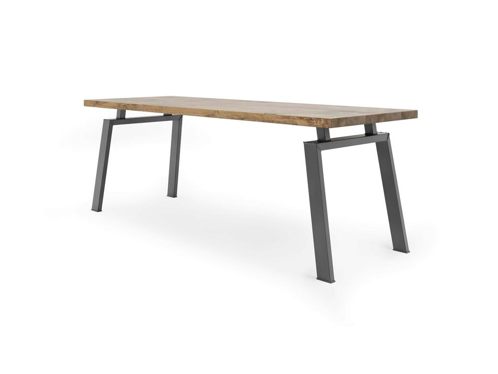 The Fulton Desk - Harvest Wheat by James+James is a modern rectangular table featuring a wooden top and angular gray metal legs that tilt outward, giving it a unique and sturdy appearance. The tabletop exhibits a light wood color with a natural wood grain pattern.