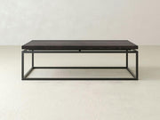 A rectangular coffee table, the "Floating Top Coffee Table - Charred Ember" by James+James, features a dark wooden top paired with a minimalist black metal frame. The table boasts a simple, modern design and is set against a plain, light-colored background.